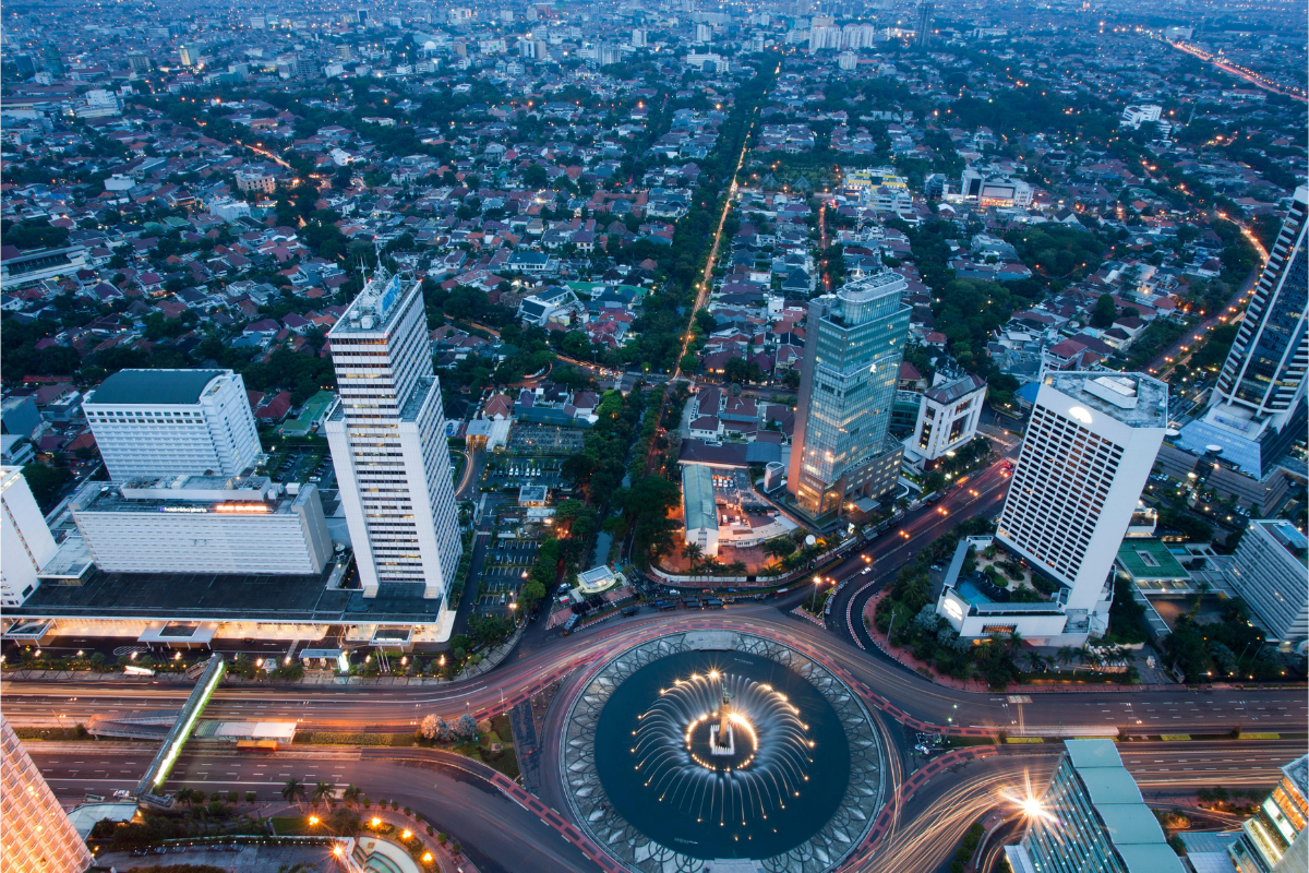 Panoramiczne ujęcie centrum Jakarta o zmierzchu – widok z lotu ptaka na rondo z fontanną pośrodku, otoczone wieżowcami