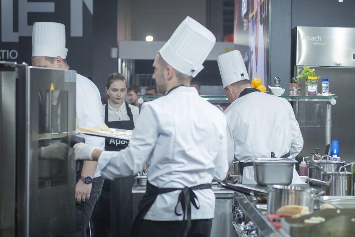 Kilku kucharzy i kucharka krzątają się po profesjonalnej kuchni