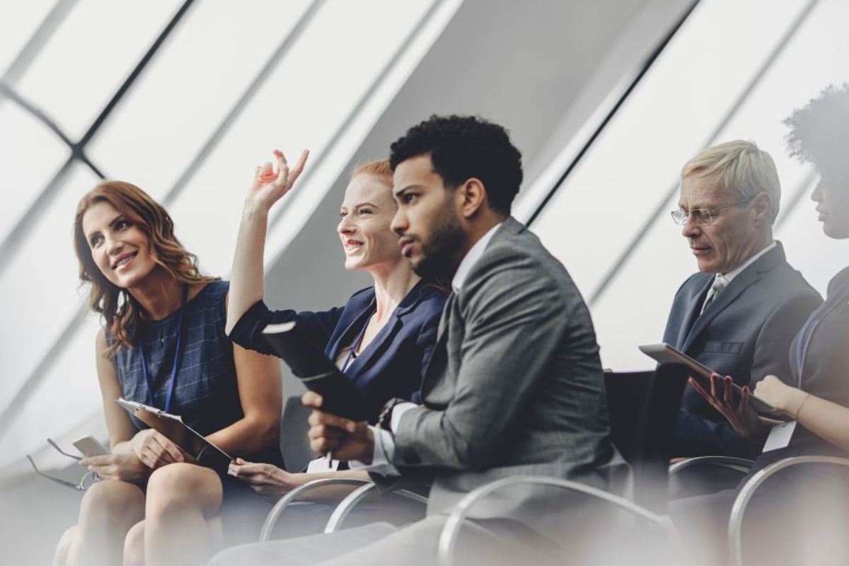 Kilka osób na krzesłach, jedna pani podnosi rękę