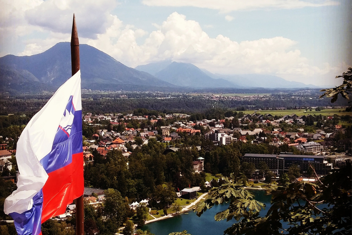 Widok na powiewającą flagę słoweńską na tle miasta i gór w tle
