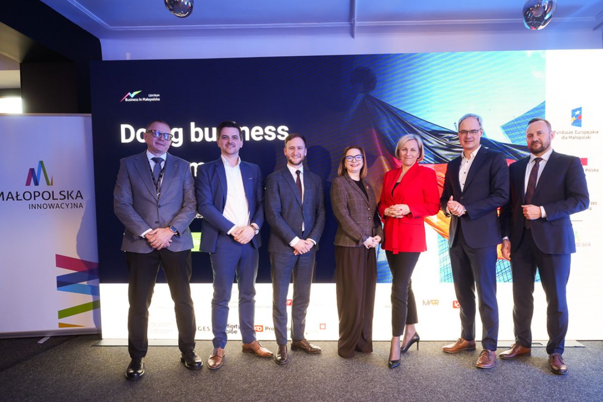 Prelegenci stojący na tle monitora